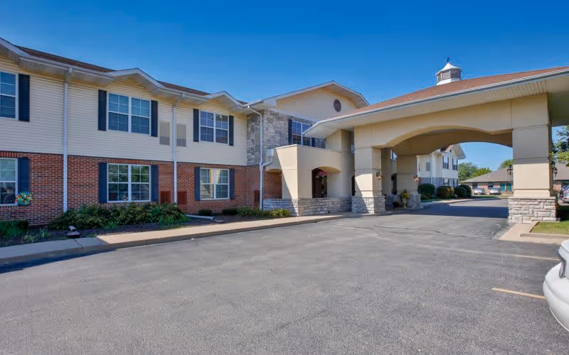 Front entrance and porte-cochère of a two-story senior living facility with brick and siding exterior and a paved driveway.