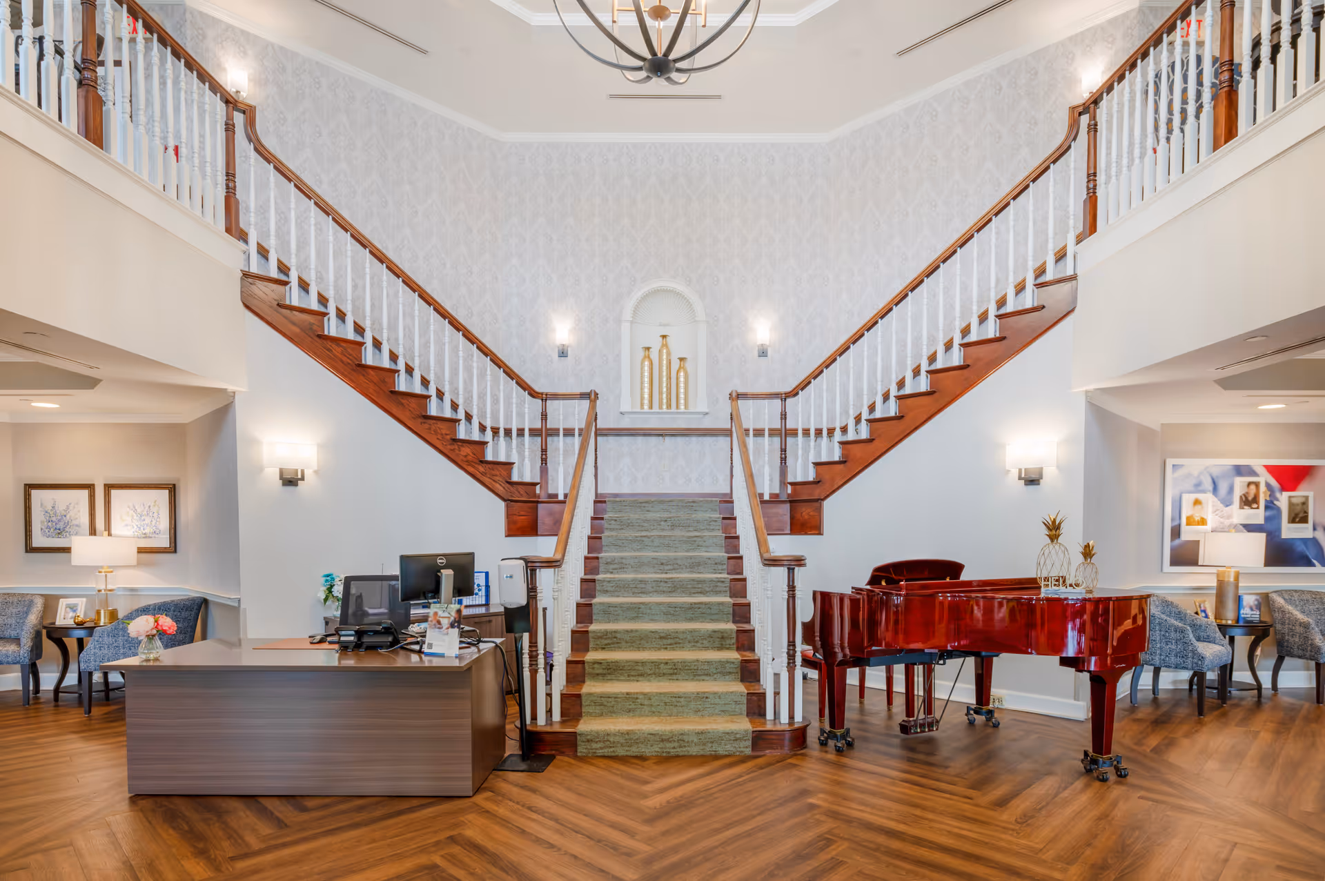 Elegant lobby with a central carpeted double staircase, reception desk, and a red grand piano.