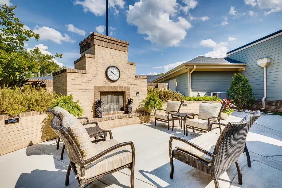 Outdoor patio courtyard with wicker lounge chairs arranged around a brick fireplace topped by a clock.