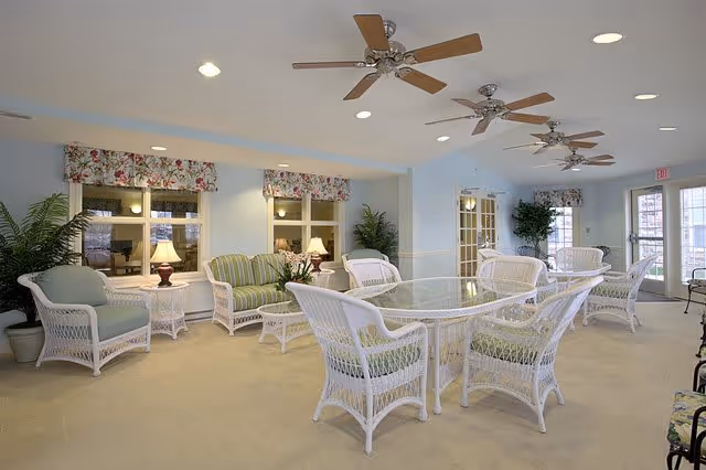 Bright communal seating area with white wicker chairs and glass-top tables, striped cushions, ceiling fans and potted plants.