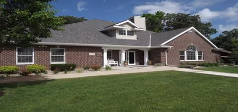 Brick senior living facility with a wide lawn, covered entrance, and a front porch.