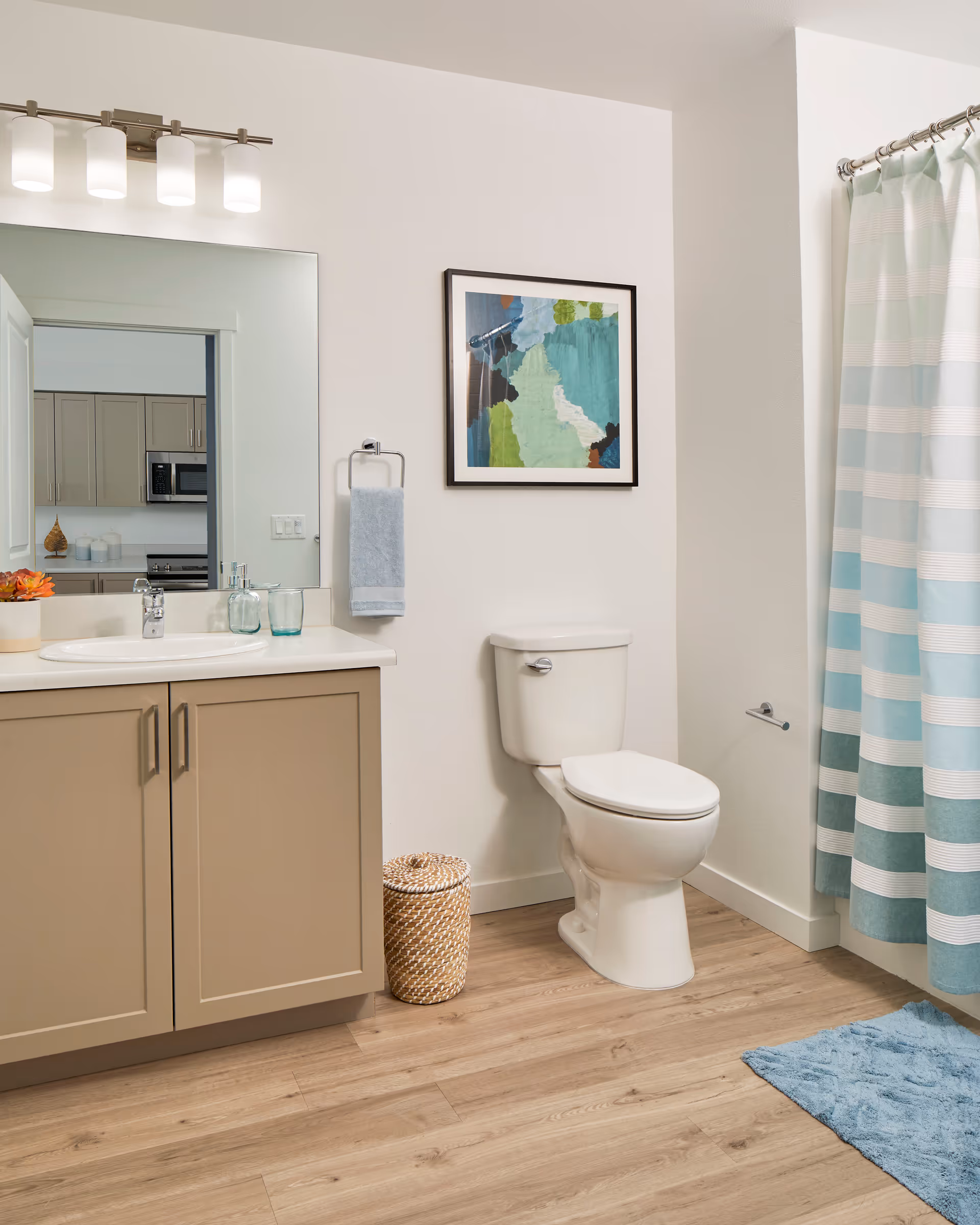 A modern bathroom with a vanity and sink, toilet, framed artwork, and a blue-striped shower curtain.