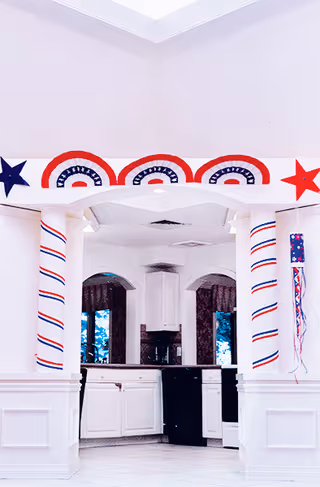 A bright interior kitchen seen through decorative columns adorned with red, white, and blue patriotic bunting and stars.