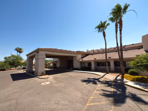 Front entrance and porte-cochère of a single-story senior living building with palm trees and a driveway.