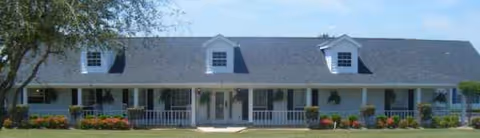 Front view of a long, single-story senior living facility with a covered porch and lawn.