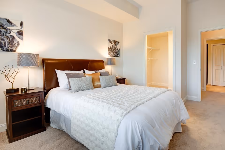 Spacious bedroom with a large bed featuring a brown headboard, nightstands with lamps and decorative pillows, and an open walk-in closet.