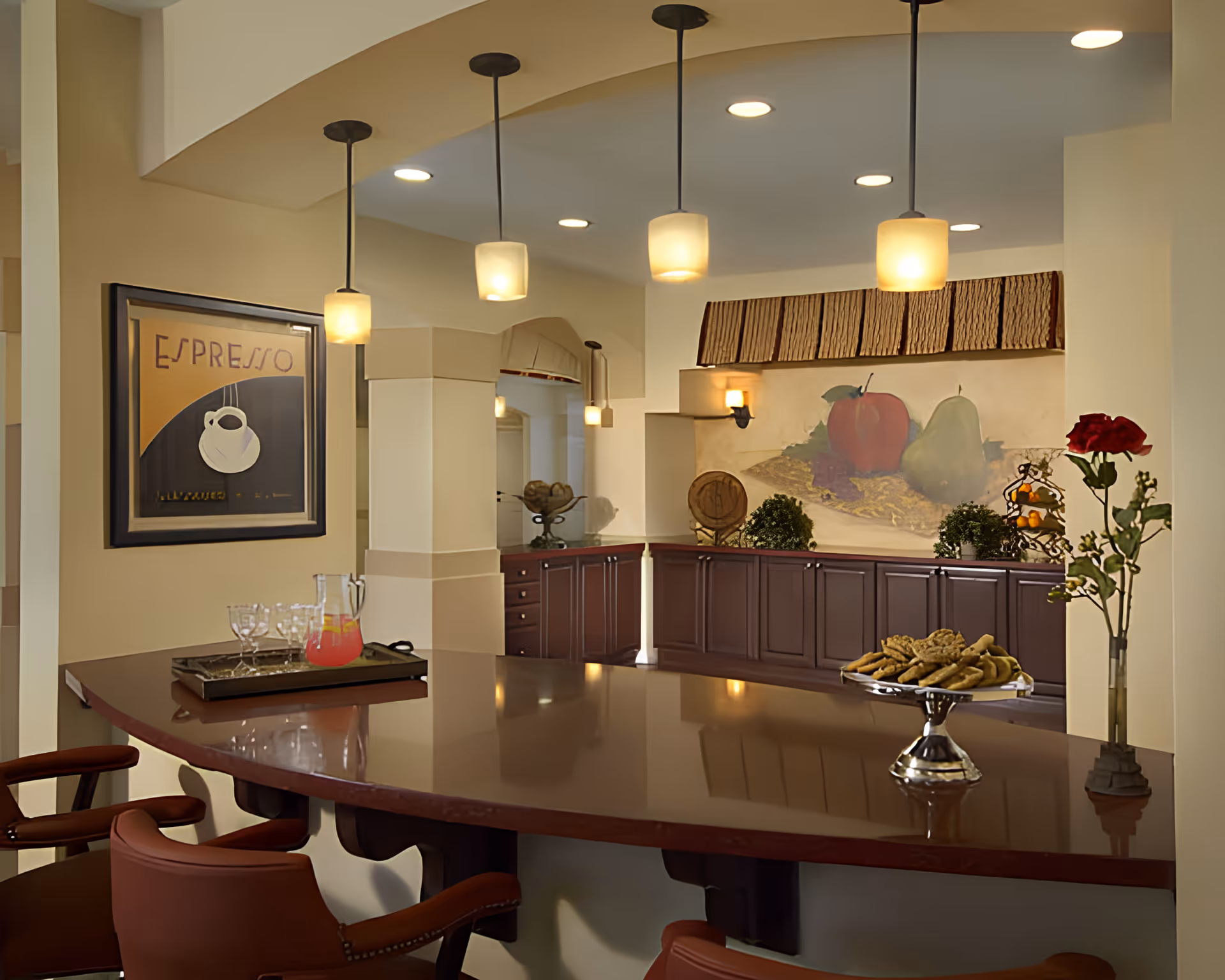Interior view of a communal dining/bar area with a polished counter, pendant lights, seating, framed espresso art, and a fruit mural.