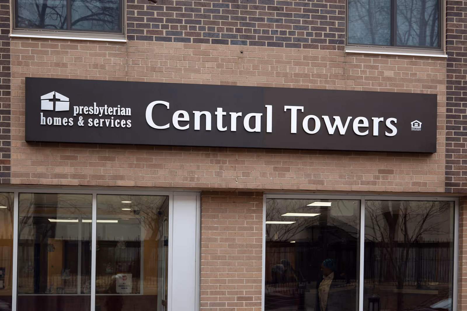 Exterior view of a brick building with a black sign that reads 'presbyterian homes & services Central Towers' above glass doors and windows.