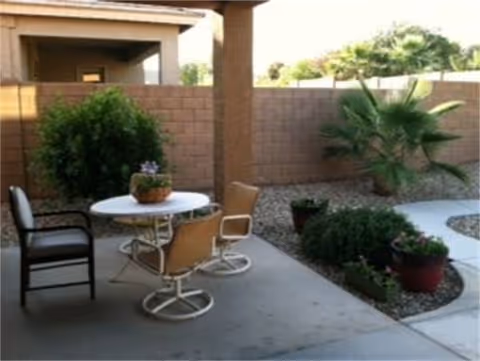 Outdoor patio at Lynne's Assisted Living with a round table, chairs, and potted plants.