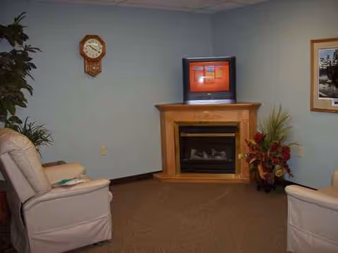 Two white recliner chairs face a fireplace with a TV on the mantle in a lounge.