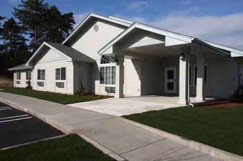 White assisted living facility exterior with a covered entrance and manicured lawn.