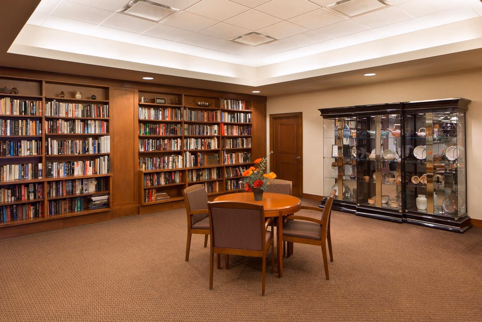 A cozy interior reading room with built-in bookshelves, a round table and chairs, and a glass display cabinet.
