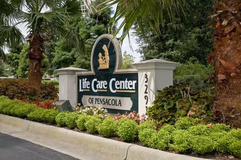Exterior view of the Life Care Center of Pensacola sign surrounded by landscaping and palm trees.