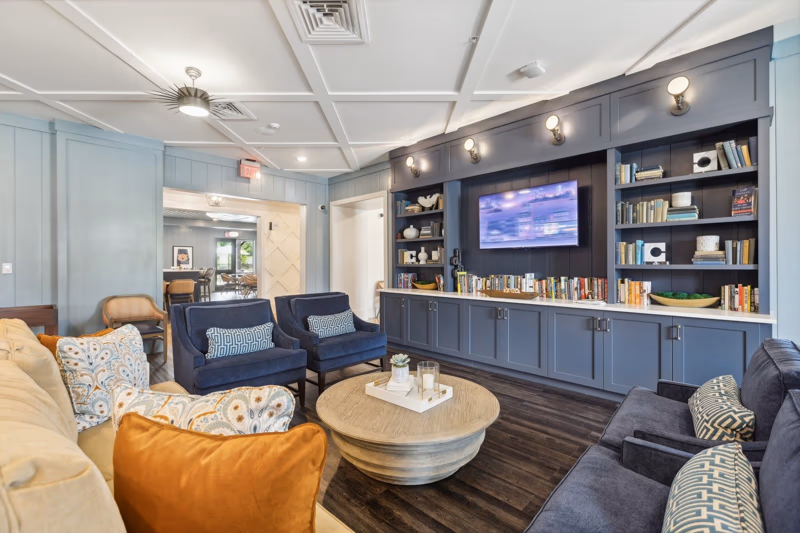 Cozy common living room with sofas and armchairs around a round coffee table, built-in shelving and a wall-mounted TV.