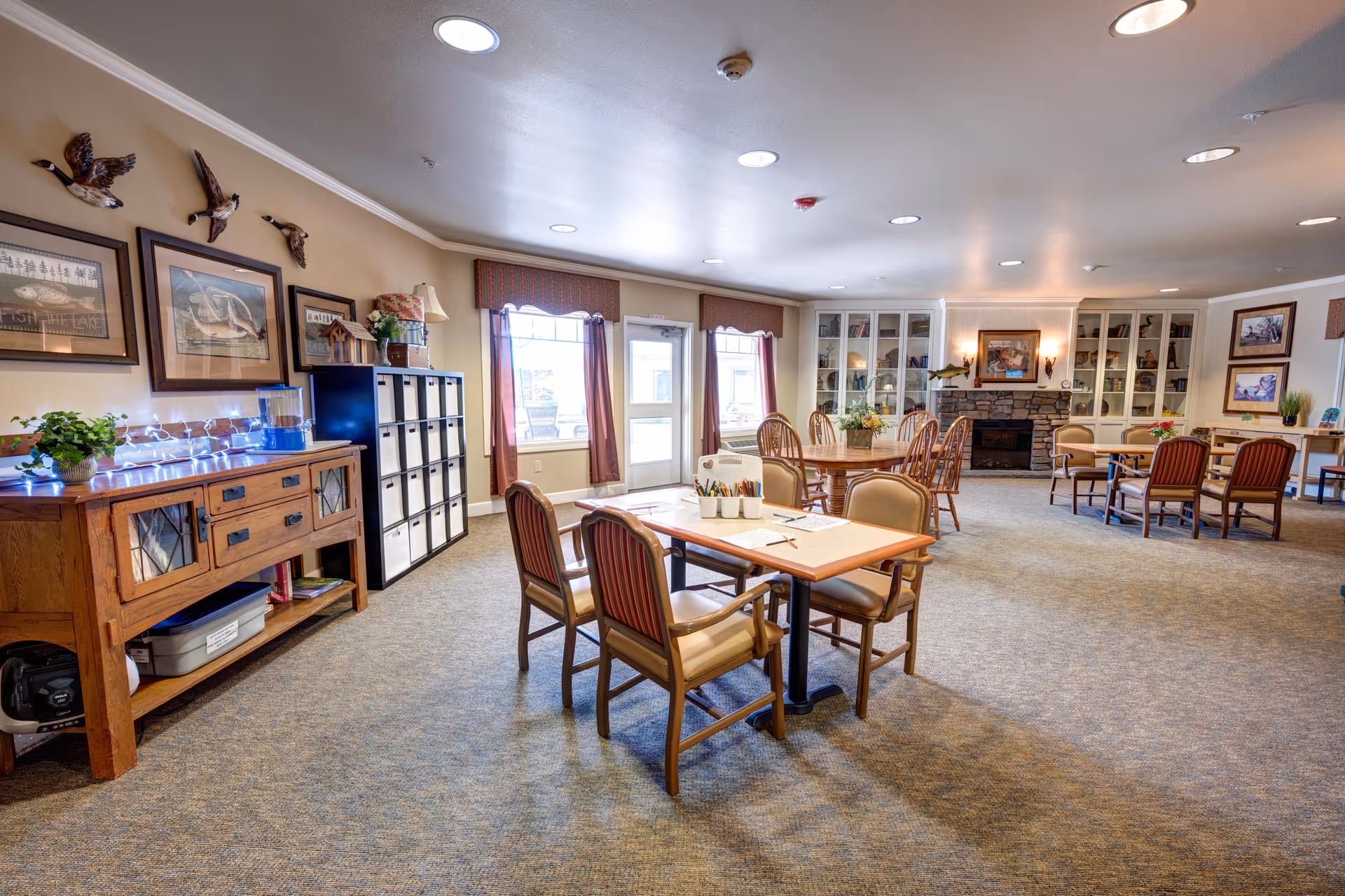 Spacious senior living common area with tables, chairs, and a fireplace.