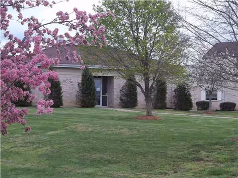 Exterior view of a senior living center with trees and a green lawn.