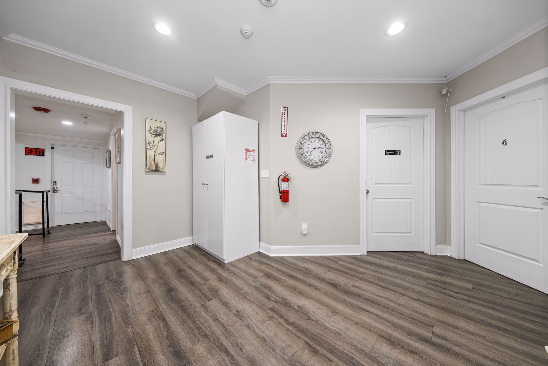 Interior hallway with wood-look floors, multiple white doors, a wall clock, and a mounted fire extinguisher.