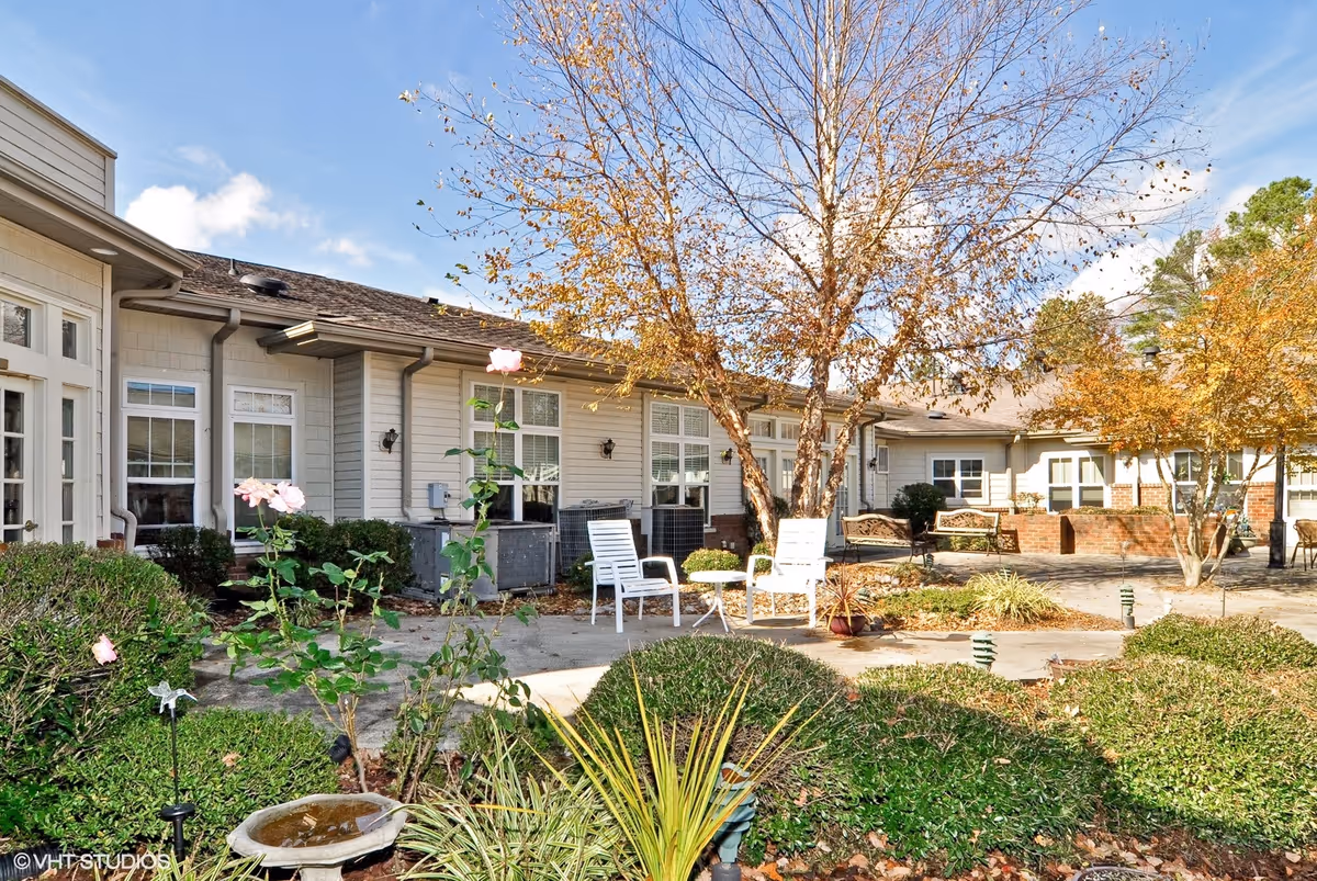 Courtyard patio with chairs, trees, and landscaping in front of a single-story senior living building.