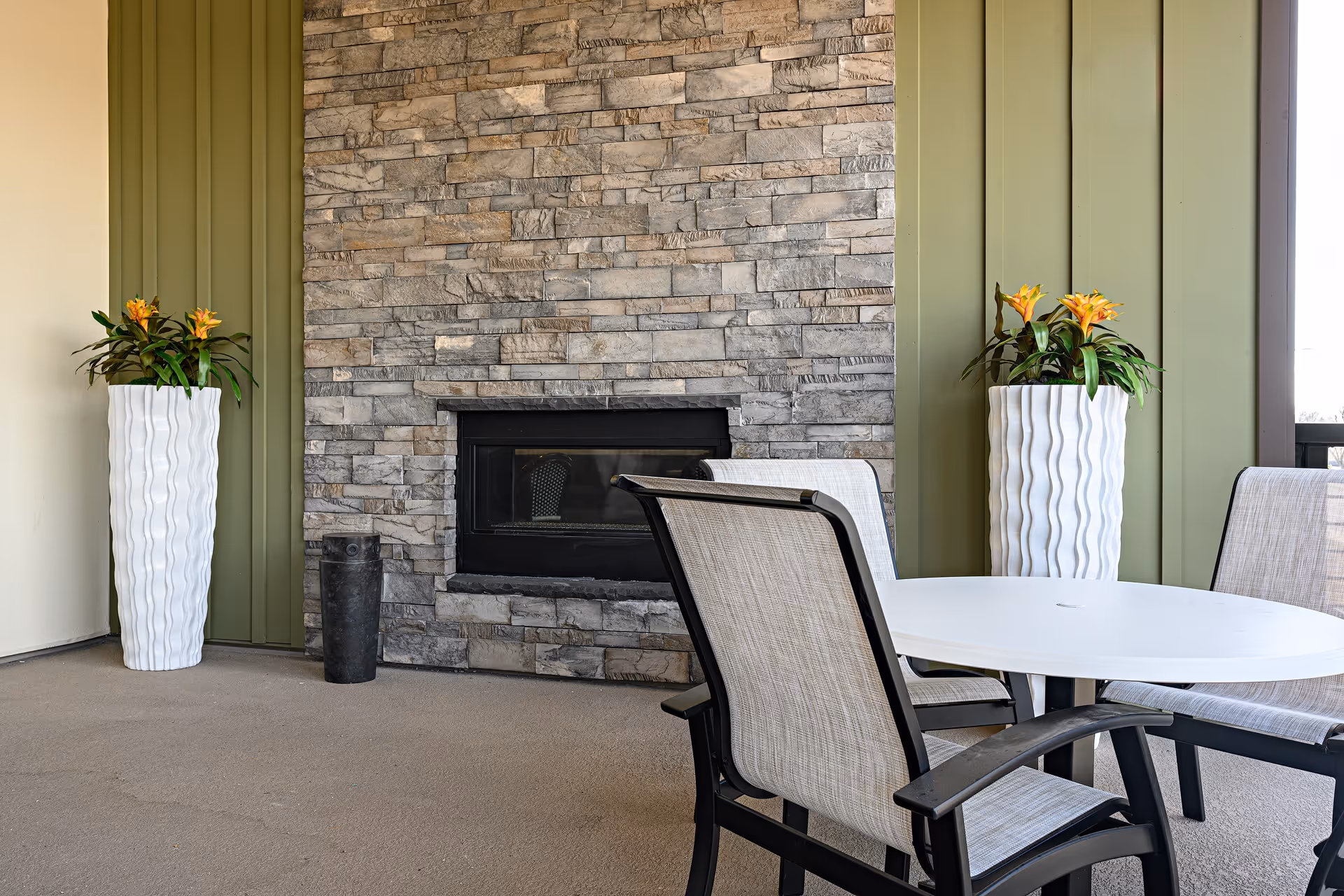 Round white table and chairs in a seating area next to a stone fireplace flanked by two tall white planters with yellow flowers.