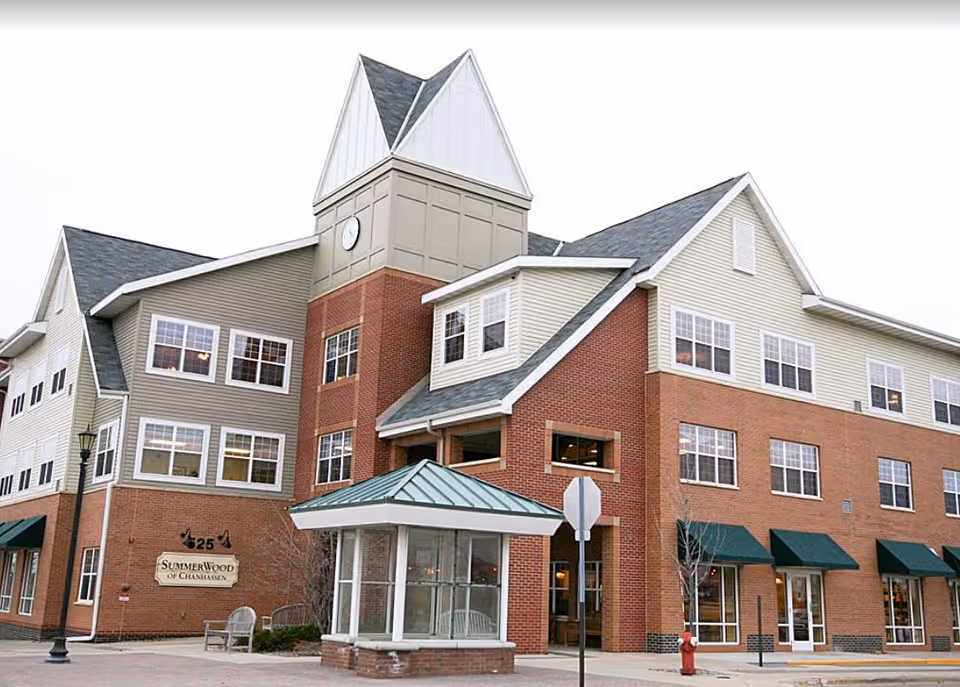 Front exterior of a multi-story brick-and-siding senior living building with a tower, entrance canopy, and a sign for SummerWood of Chanhassen.