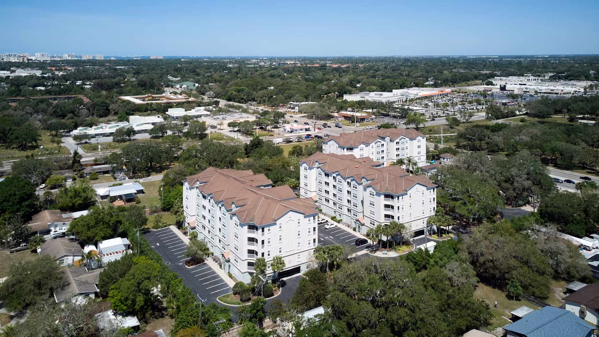 Aerial view of Arietta senior living buildings with brown roofs, parking lots, and surrounding trees.