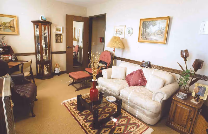 Cozy living room with a cream sofa, upholstered chairs, a patterned rug, a glass-front display cabinet, and decorative lamps and wall art.