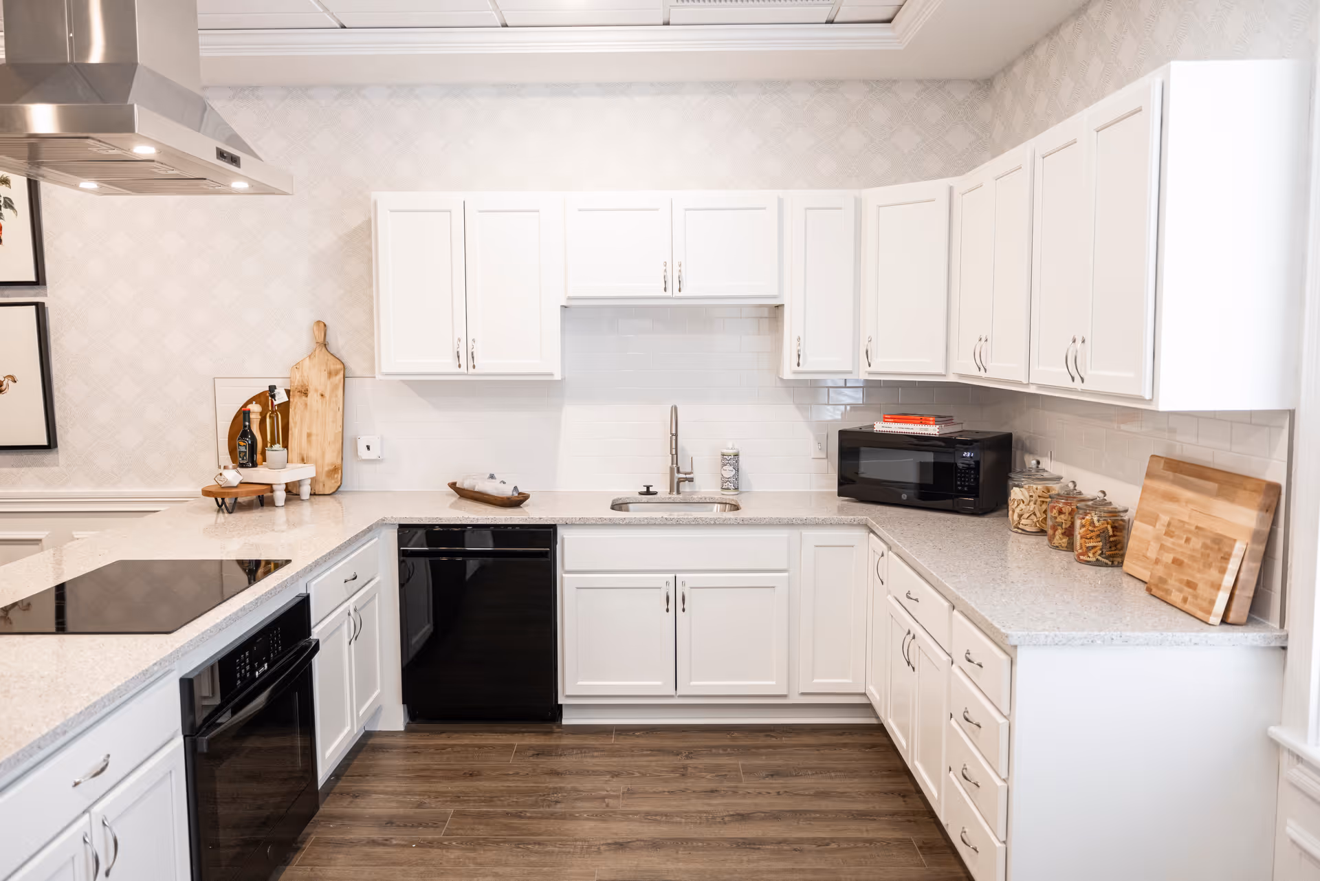 Bright modern U-shaped kitchen with white cabinets, gray countertops, stainless steel range hood, and black appliances.