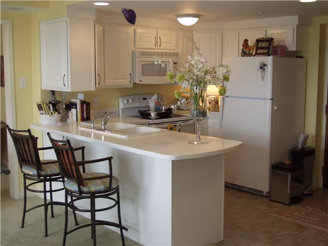Bright open kitchen with white cabinets, an island countertop with a sink and two barstools, and a refrigerator.