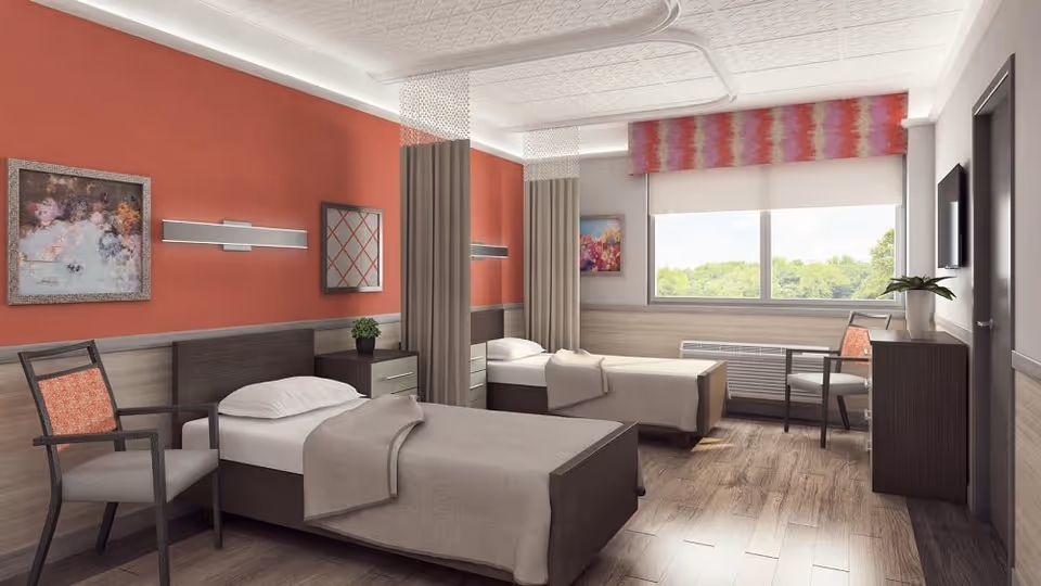 A bright and clean bedroom with two single beds separated by a nightstand with a small plant. Each bed has beige bedding and a pillow. There are two chairs with patterned cushions, one near each bed. The walls are painted a warm red with a wooden panel halfway up, decorated with framed artwork and modern wall lights. A large window with a colorful valance lets in natural light and shows greenery outside. The floor is wooden, and there is a TV mounted on the wall opposite the beds.