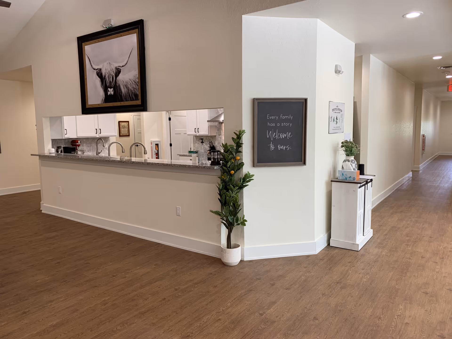 Open interior hallway with a long serving counter and kitchen pass-through, a potted plant, and a framed welcome sign on the wall.