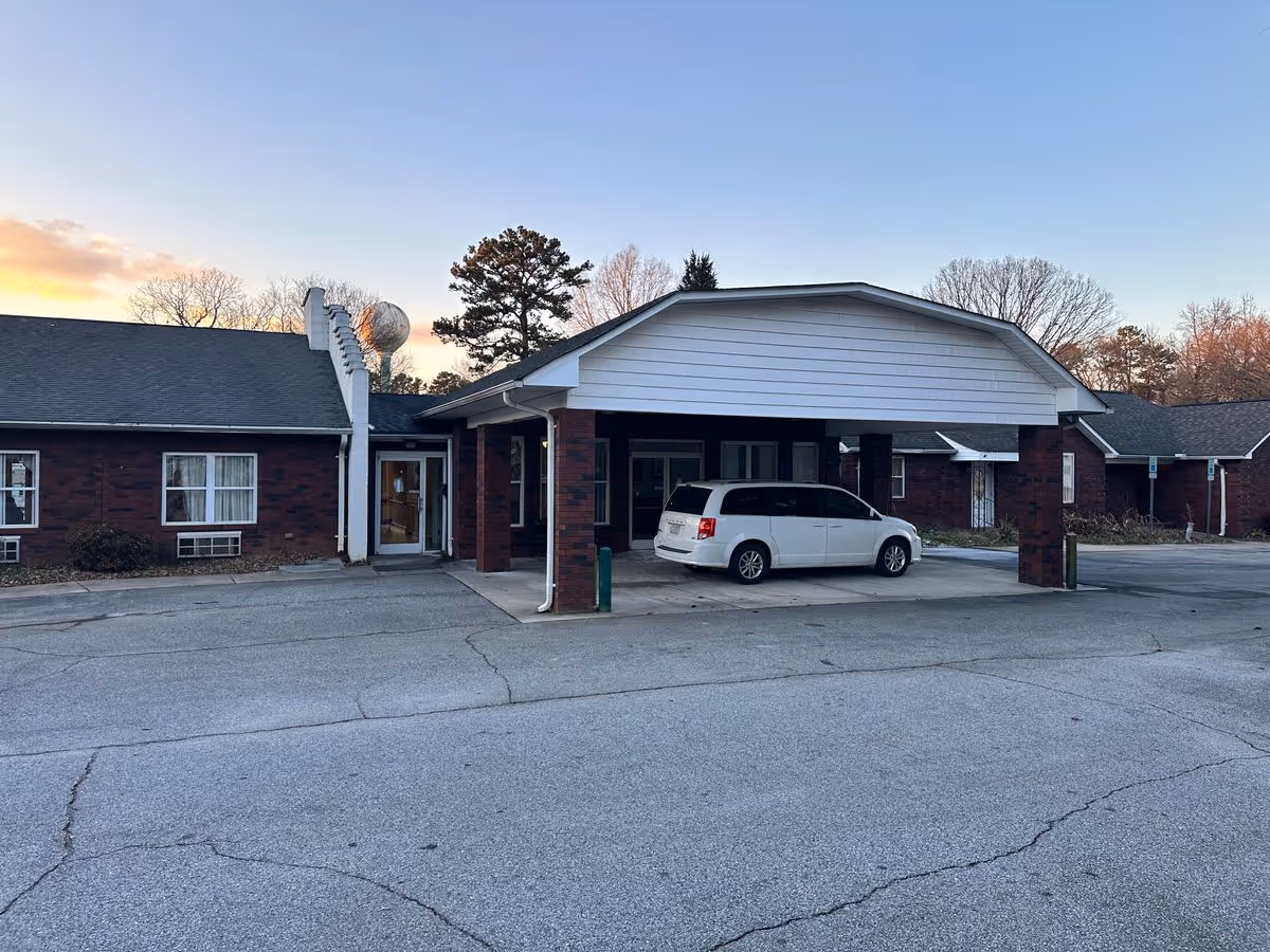Brick single-story retirement facility front entrance with a covered porte-cochere and a white minivan parked underneath.