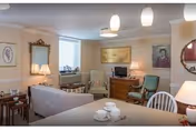 Cozy communal living room with a sofa, armchairs, dining table, lamps, and wall art.