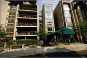 Exterior view of a multi-story residential building with balconies, greenery, and a green canopy over the entrance walkway.