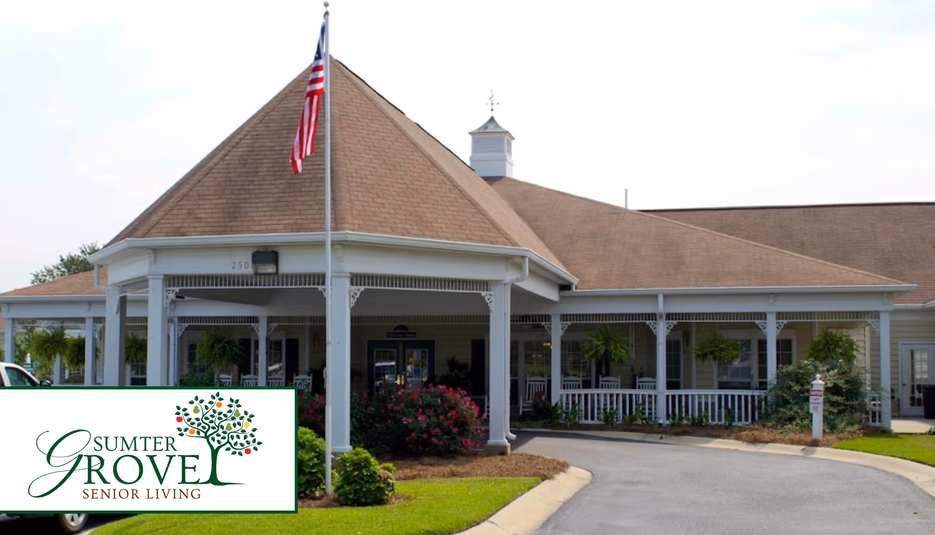 Front entrance of Sumter Grove Senior Living with a covered porch, flagpole, and landscaped driveway.