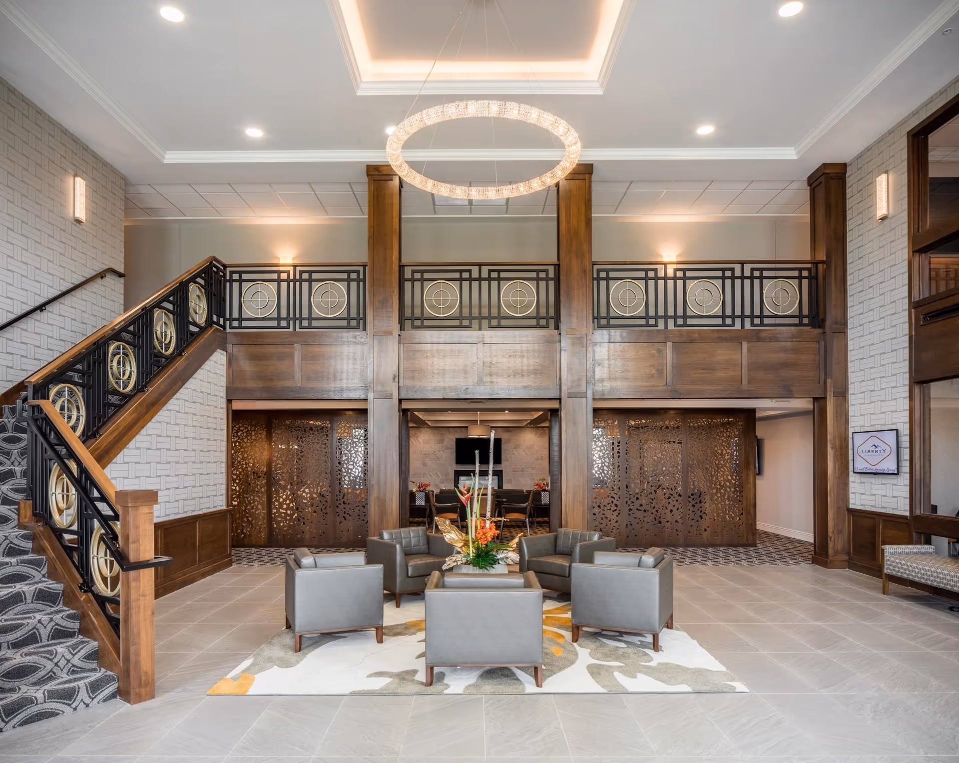 Spacious two-story lobby with a circular chandelier, a central seating area, decorative staircase, and wood-paneled balcony.