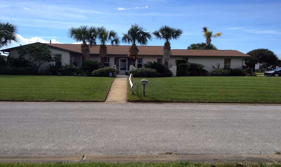 Single-story ranch-style building with palm trees, a central walkway, and a neatly mowed front lawn.