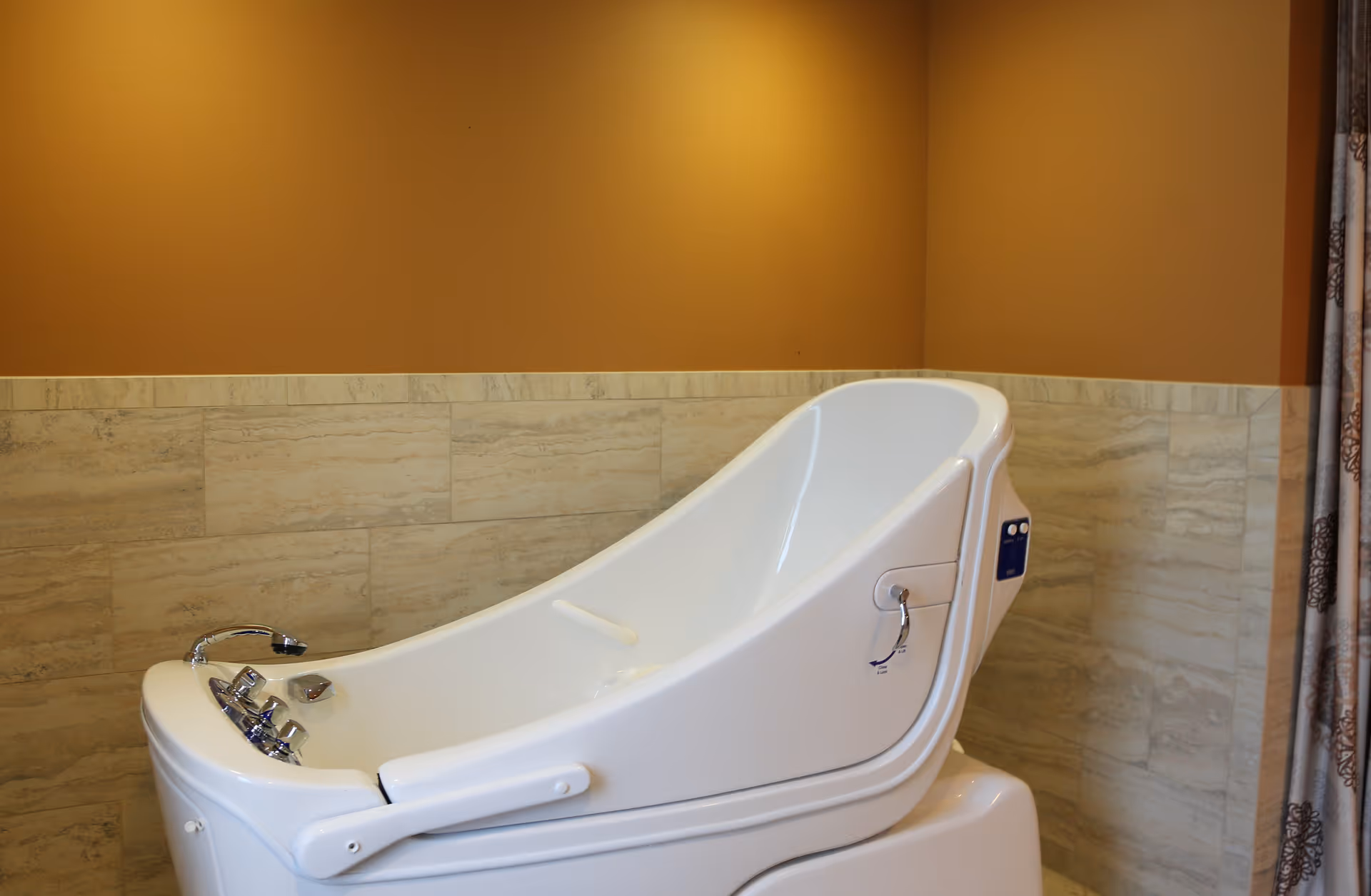 A white assisted bathing tub in a tiled bathroom with warm tan walls.