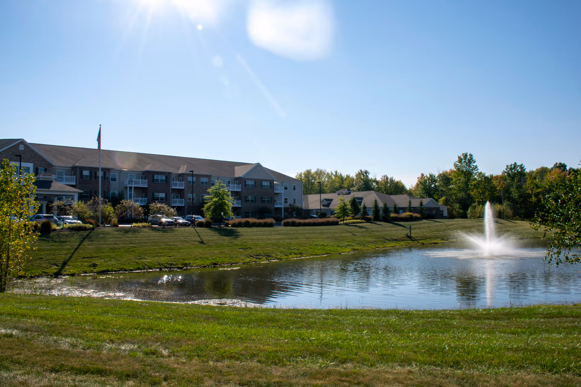 Exterior view of the Springwood Hudson building with a pond and fountain in the foreground under a clear blue sky.