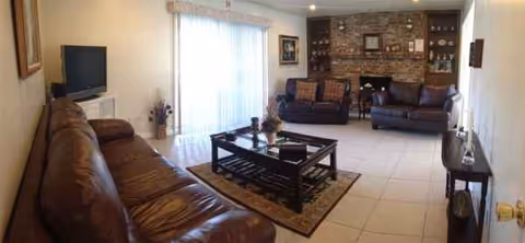Spacious living room in a senior facility featuring leather sofas, stone fireplace, and sliding doors.