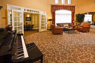 Lounge area at Laurel Court senior facility with plush seating, a piano, and French doors.