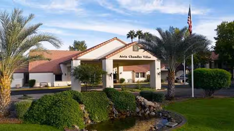 Exterior view of Atria Chandler Villas entrance with palm trees and landscaped grounds.