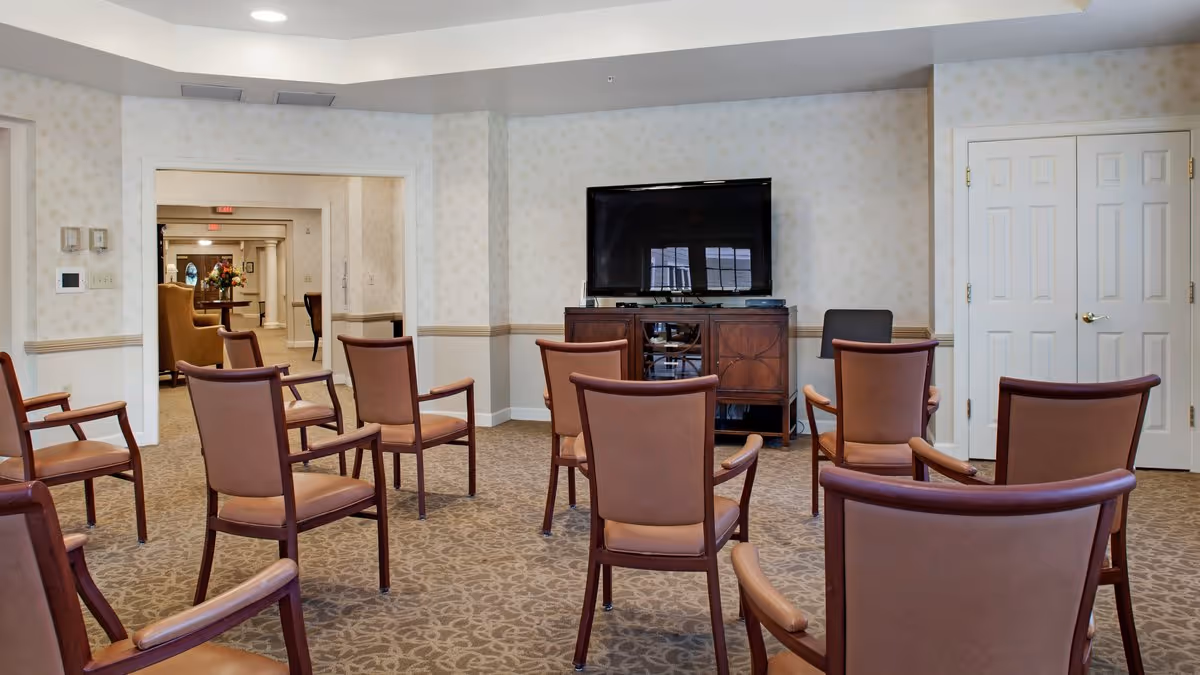 A common room with multiple brown upholstered chairs arranged in rows facing a television on a console.