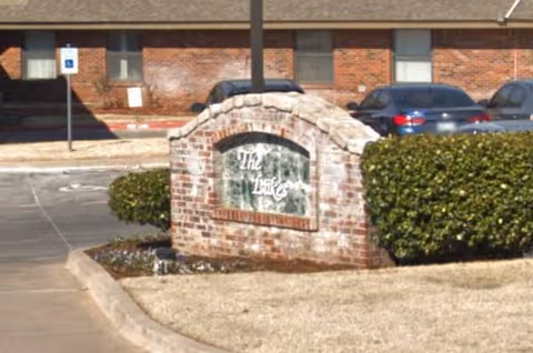 Brick sign reading The Lakes in front of a senior living facility entrance.