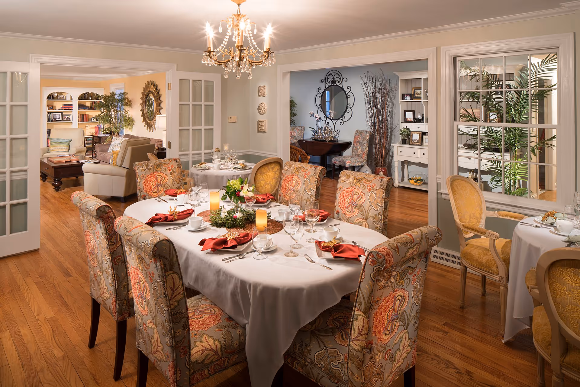 Formal dining room with a round table set for a meal, patterned upholstered chairs, a chandelier, and views into adjacent living spaces.