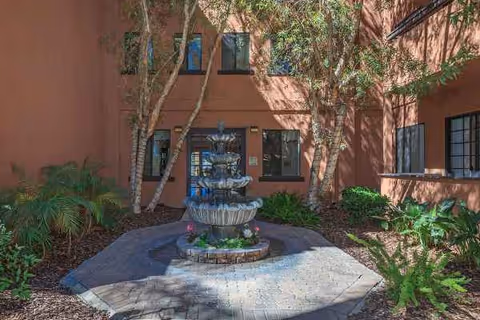 Red-orange stucco building surrounds a central courtyard with a tiered fountain and greenery.