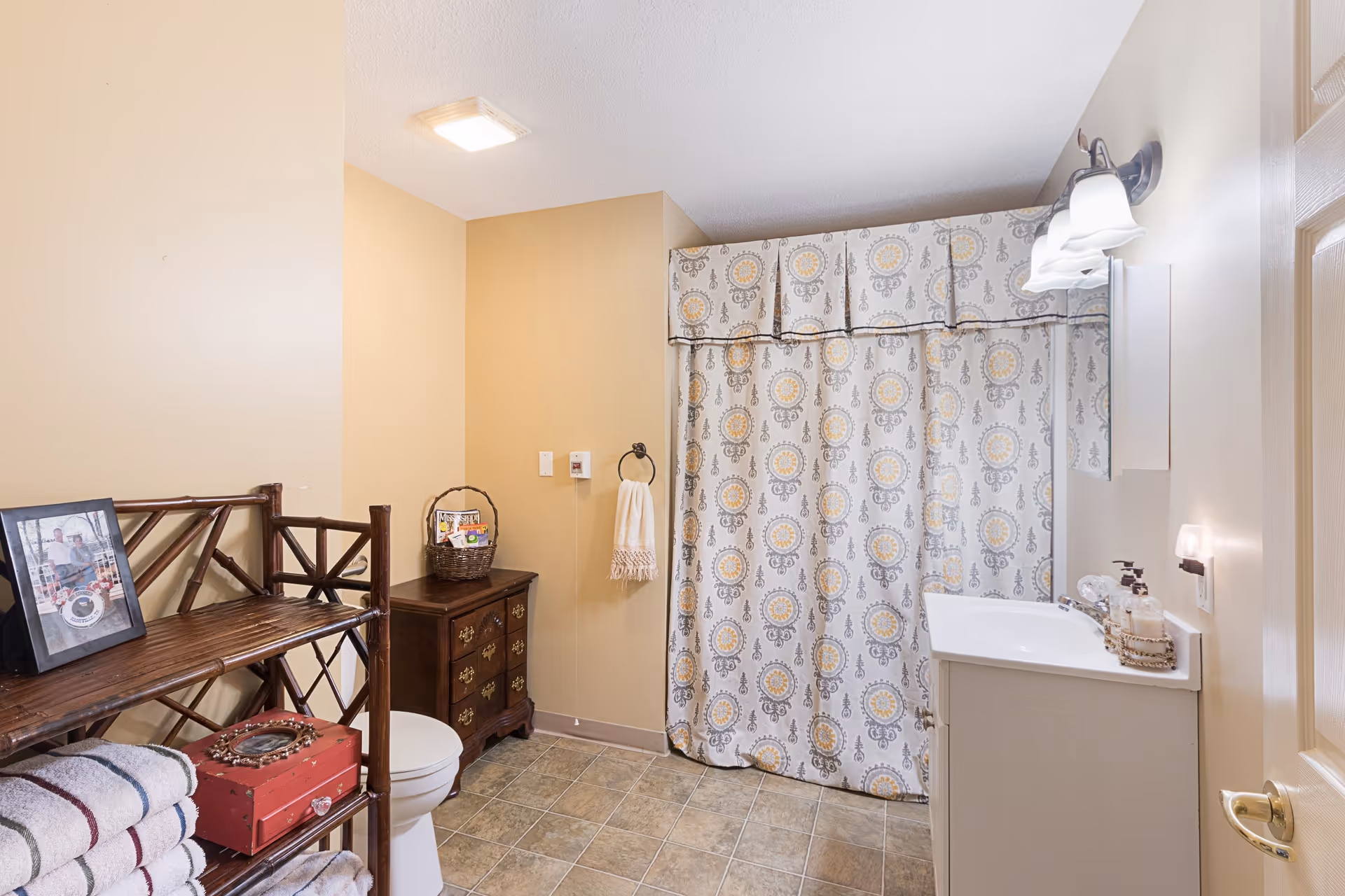 Bathroom with shower curtain, sink, toilet, and towels in a senior living facility.