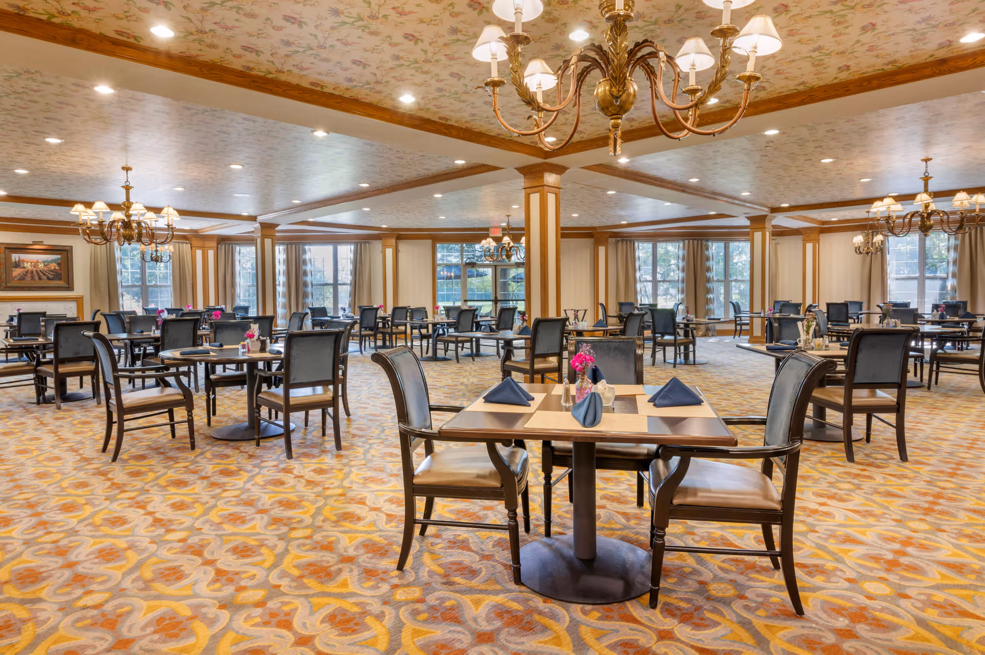 Large, elegant dining room with multiple set tables and chairs, chandeliers, and patterned carpeting.