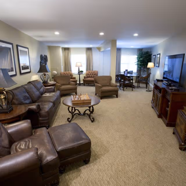 Furnished communal living room with leather sofas, armchairs, a coffee table with a chessboard, dining area and TV.