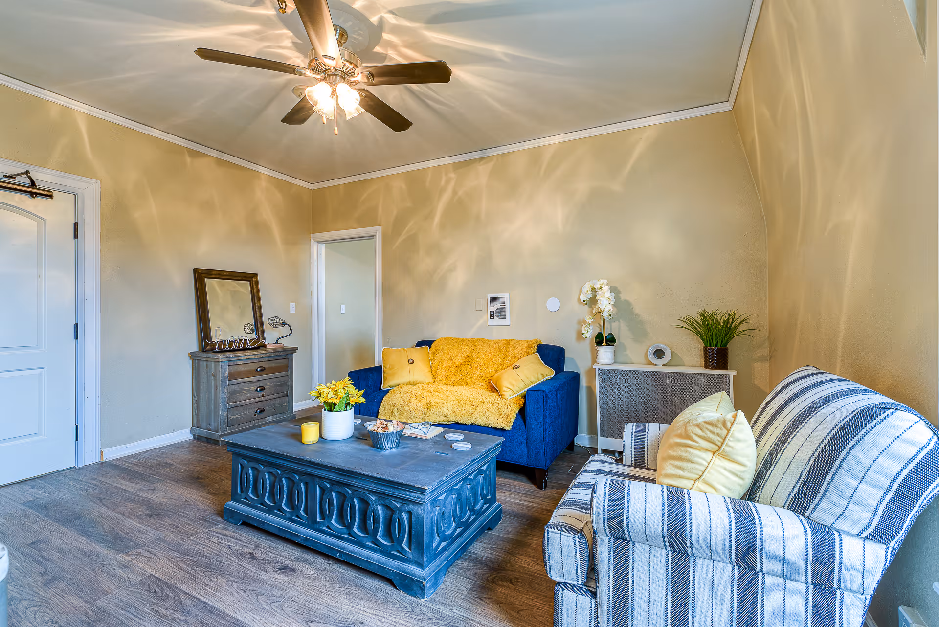 Cozy living room with a blue sofa, striped armchair, central coffee table, and ceiling fan.