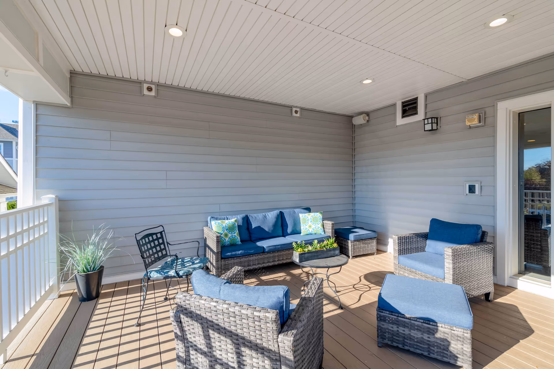 Covered outdoor patio with wicker seating, blue cushions, small table and potted plant.